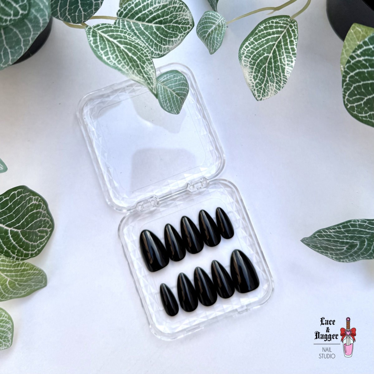 Set of Almond handmade custom black press-on nails in a clear plastic case on a white background with green leaf patterns.