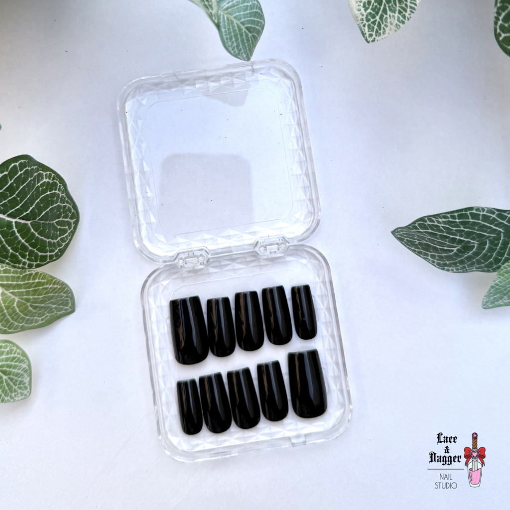 Set of Square handmade custom black press-on nails in a clear plastic case on a white background with green leaf patterns.