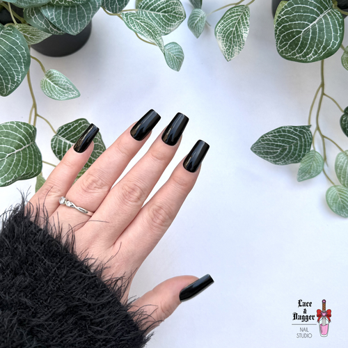 Hand with Square handmade custom black press on nails against a white background with green leaves
