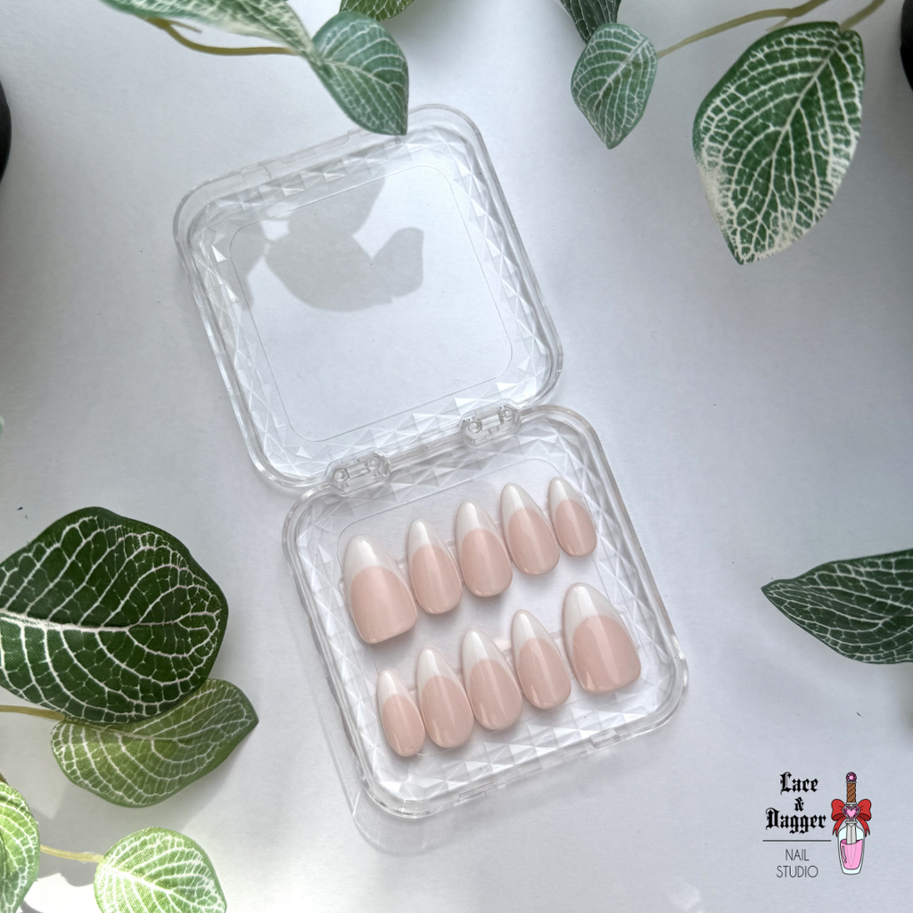 Set of almond handmade custom light pink deep french press on nails in a clear plastic case on a white background with green leaves.