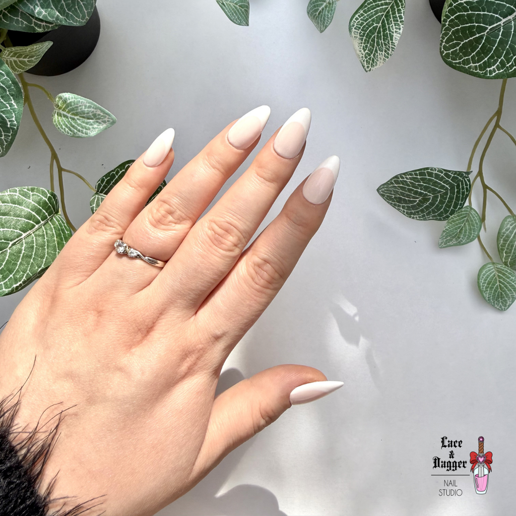 Hand with almond handmade custom light pink deep french press on nails and a ring, set against a white background with green leaf patterns.