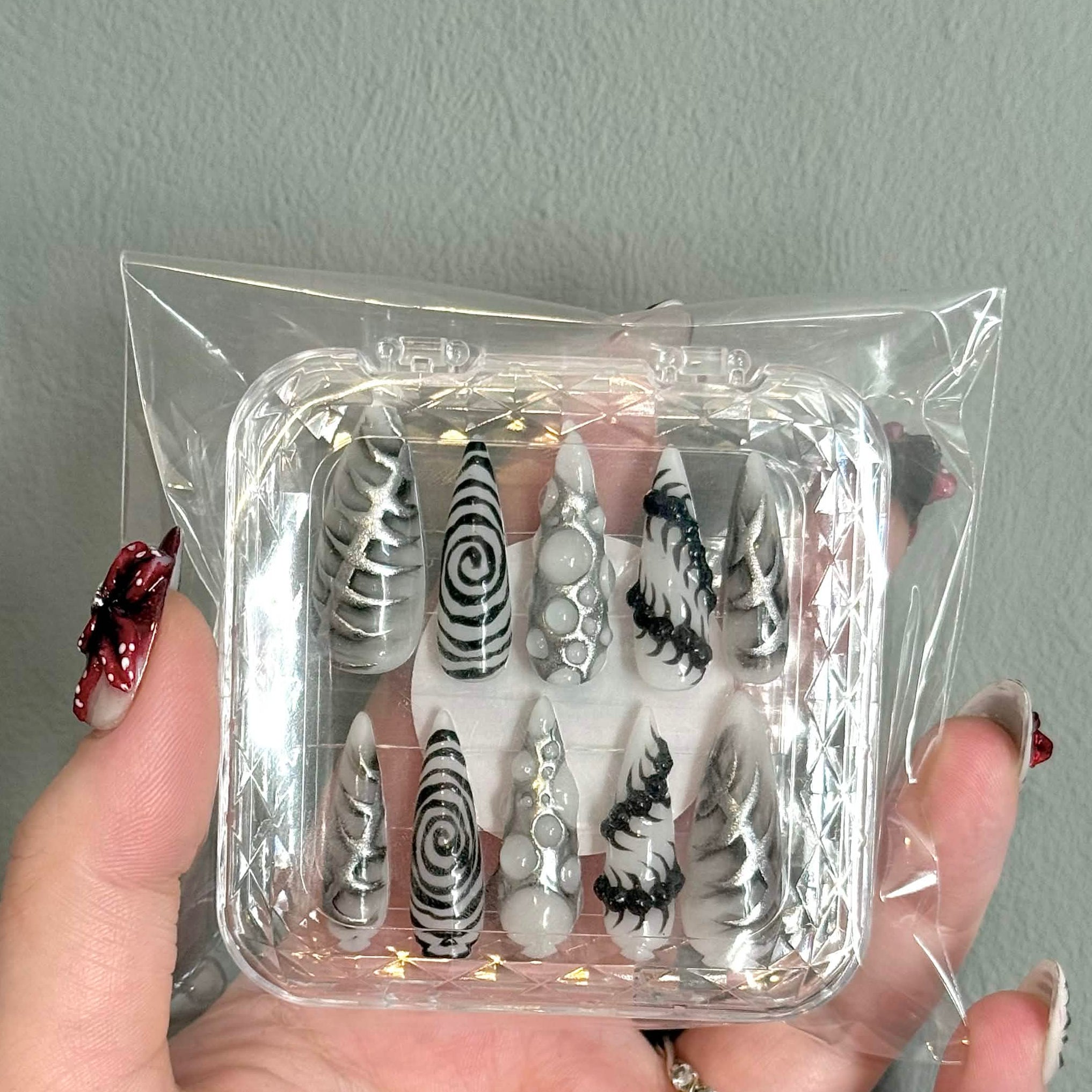 Set of black and white nail art designs in a clear plastic case held by a hand against a gray background.