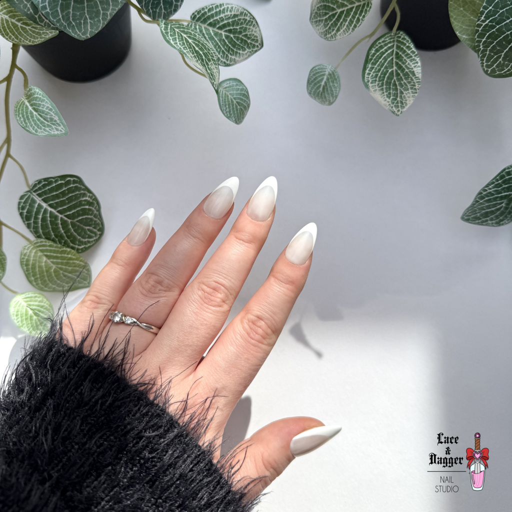 Hand with handmade custom almond milky white deep french tip press on nails on a light background with green leaves