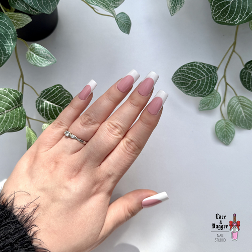 Hand with square handmade custom dark pink deep french press on nails against a light background with green leaves