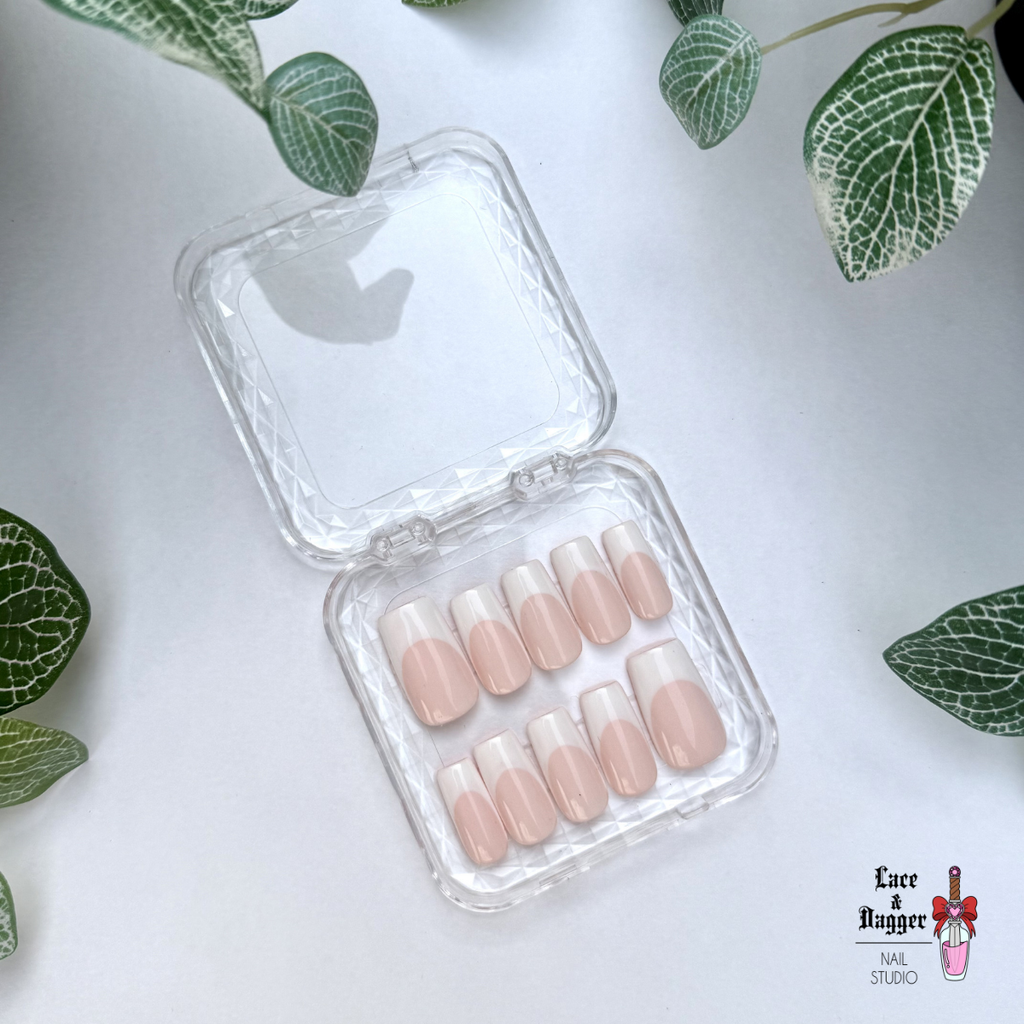 Set of square handmade custom light pink deep french press on nails in a clear plastic case on a white background with green leaves.